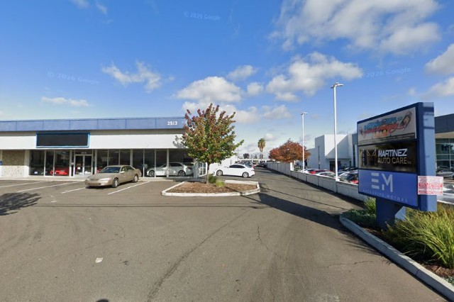 The narrow driveway off Arden Way, seen from the street: an auto shop building on the left, a Martinez Auto Care sign on the right, and cars parked along both sides.